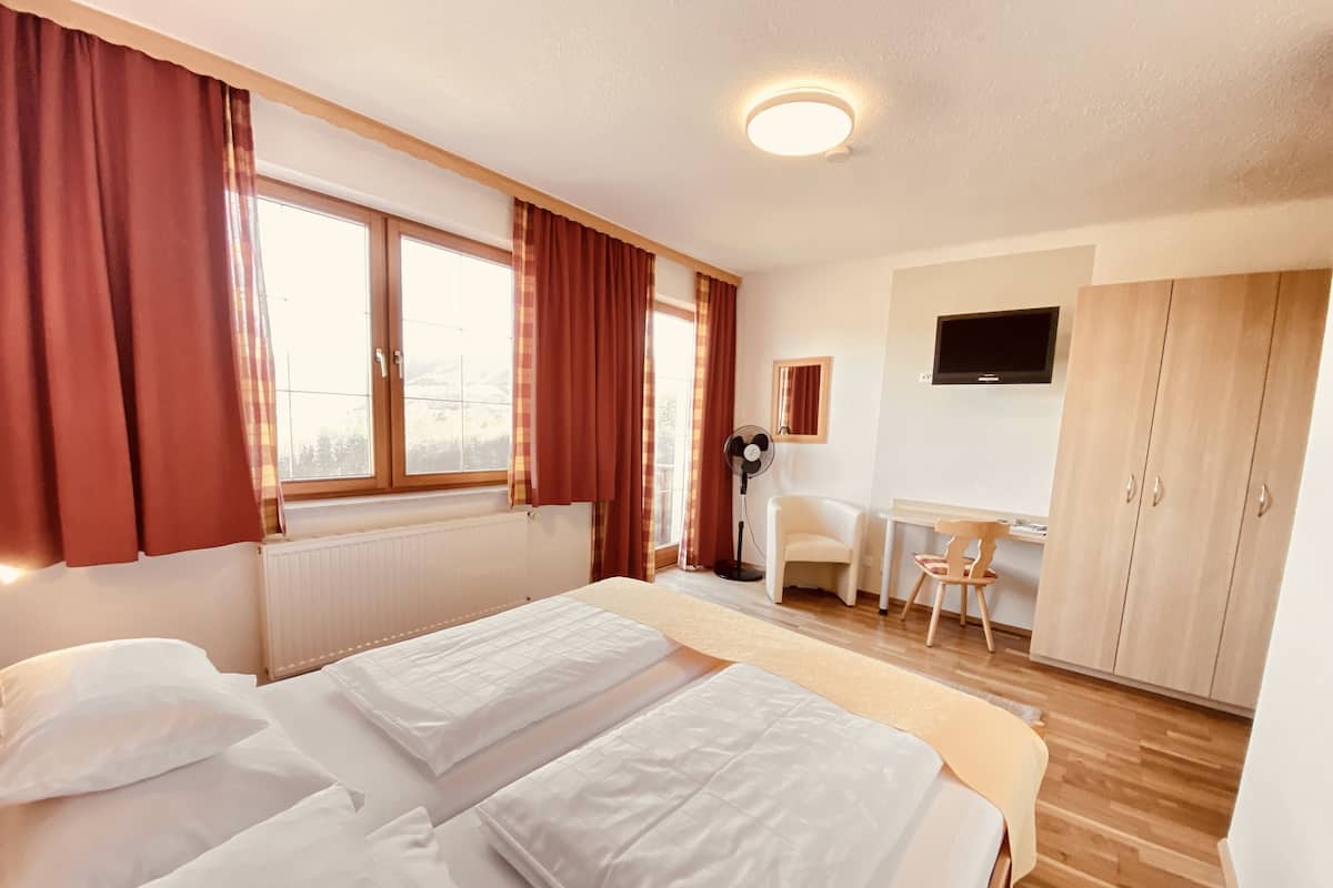A hotel room with two beds, a desk, a chair, a wardrobe, and a TV on the wall.