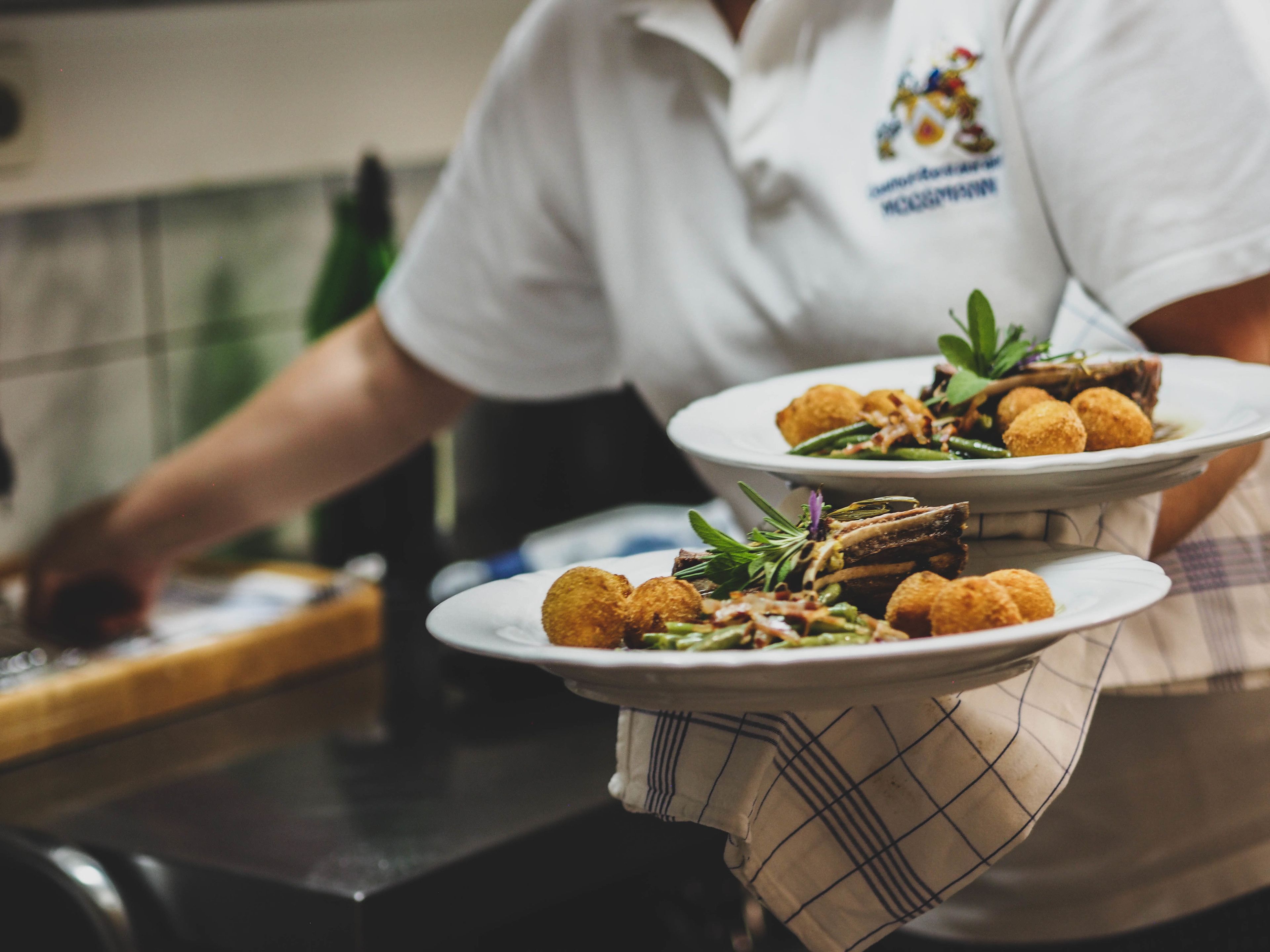 A person holding plates of food in a kitchen setting.
