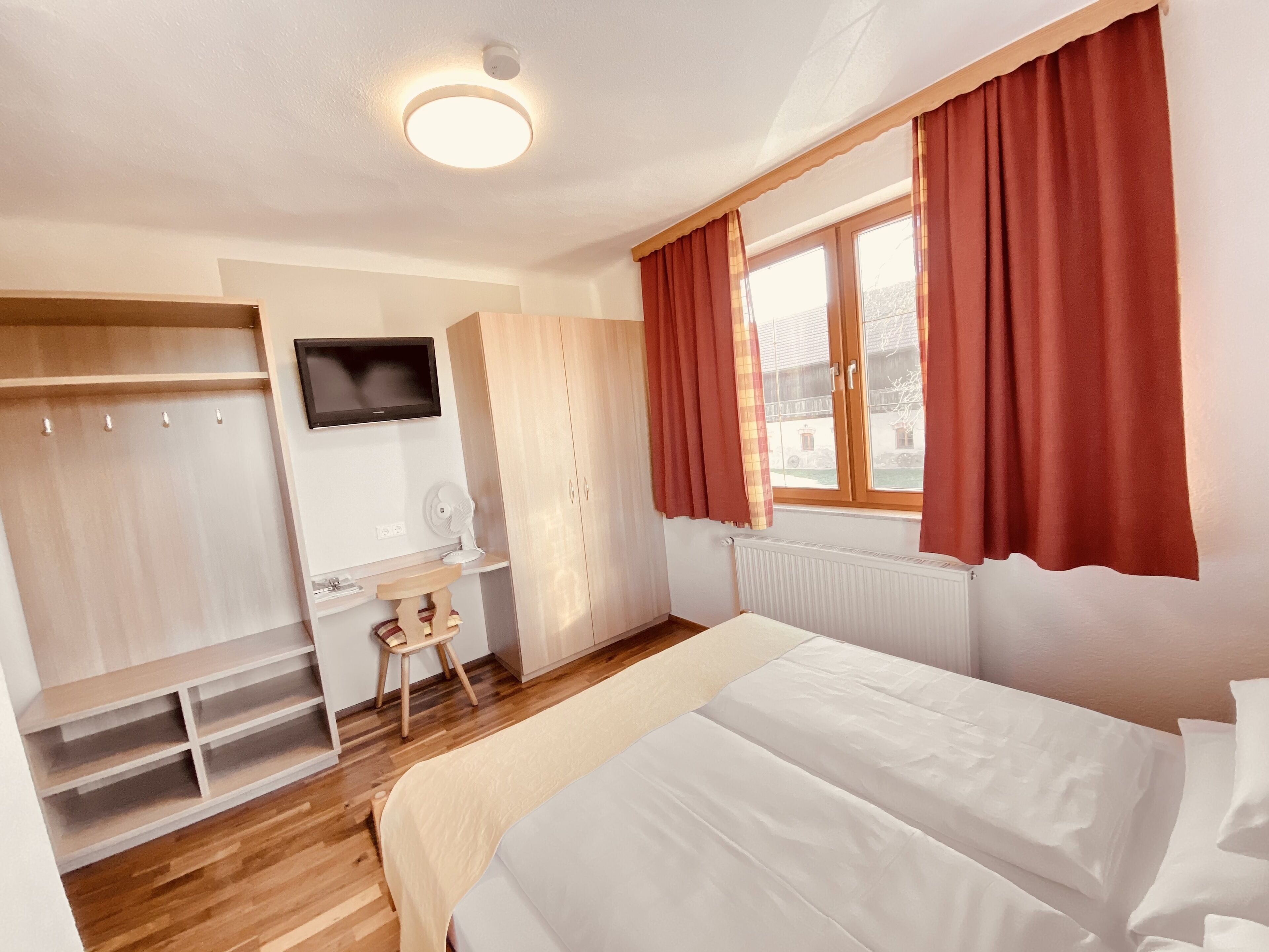 Een slaapkamer met een bed, een bureau, een stoel, een kledingkast en een raam met gordijnen.