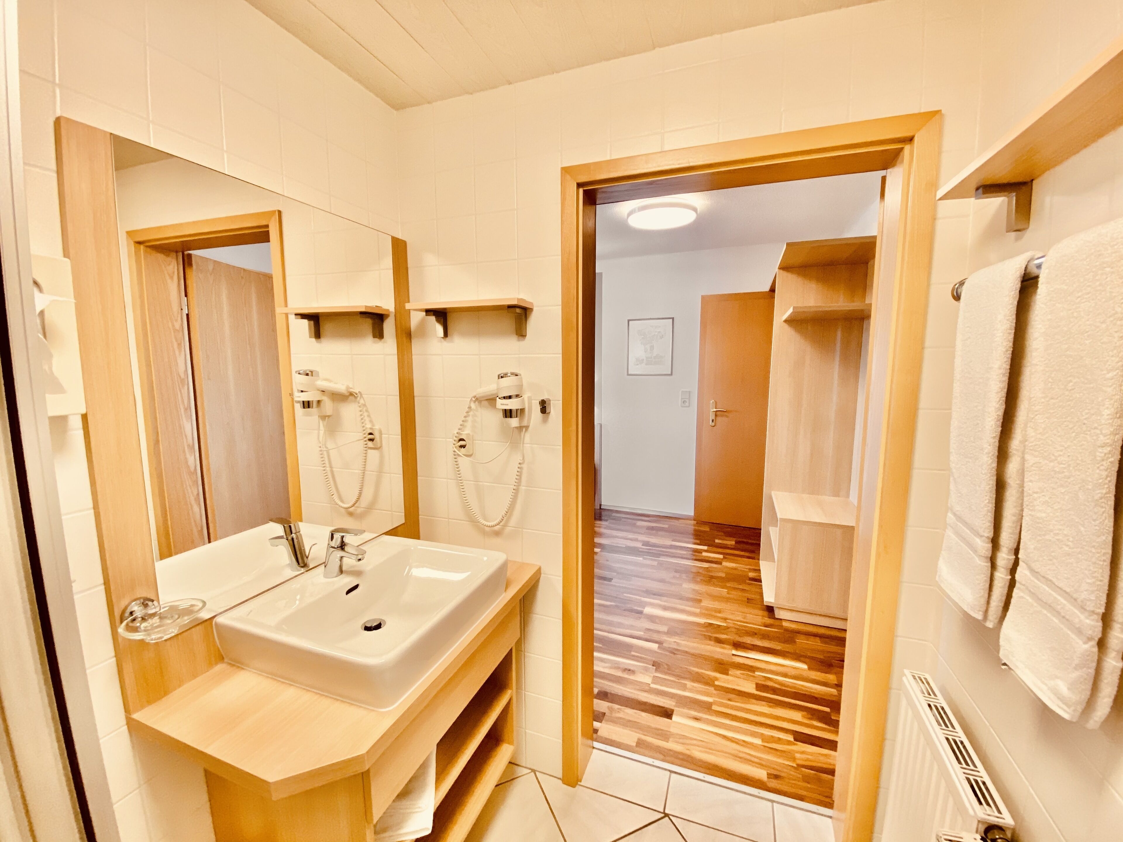 Ein modernes Badezimmer mit Waschbecken, Spiegel, Handtuchhalter und Duschbereich.