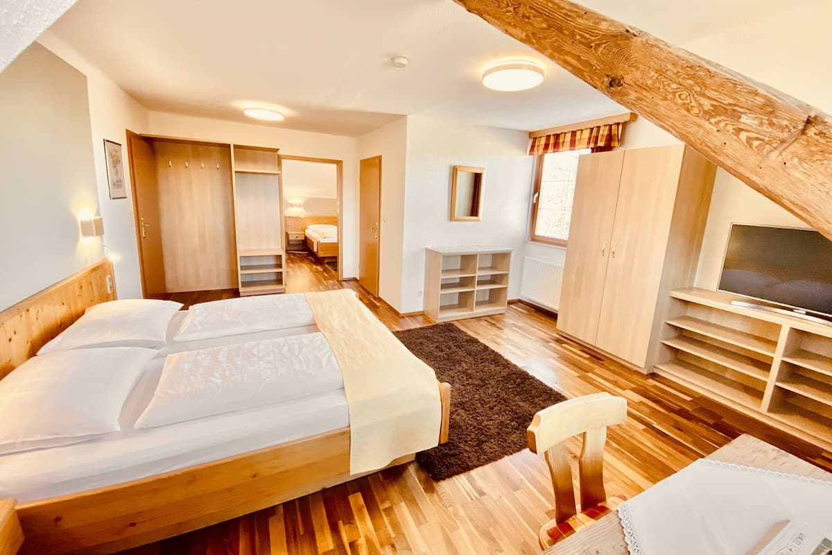 A room with a large bed, wooden flooring, a TV, and a wardrobe.