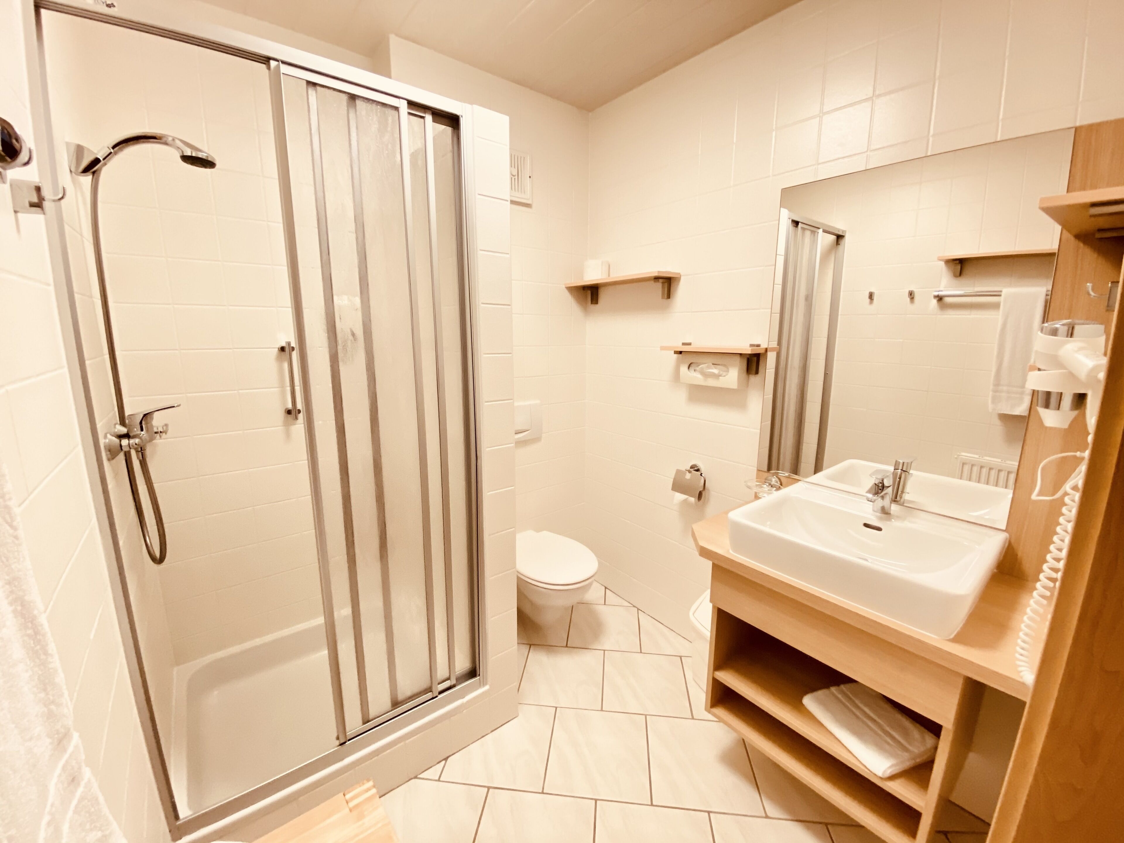 Un baño moderno con ducha de vidrio, inodoro y lavamanos sobre un mueble de madera.