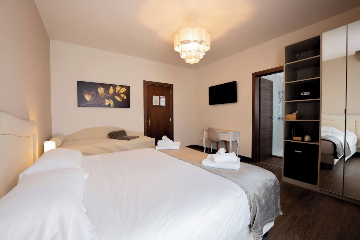 Quarto de hotel com uma cama grande, uma escrivaninha, uma cadeira, um guarda-roupa e uma televisão.