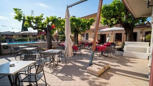 An outdoor patio with tables and chairs, a pool, and a covered seating area. - Hotel Gardenia (Sirmione)