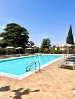 A swimming pool with a tiled deck, lounge chairs, and umbrellas.