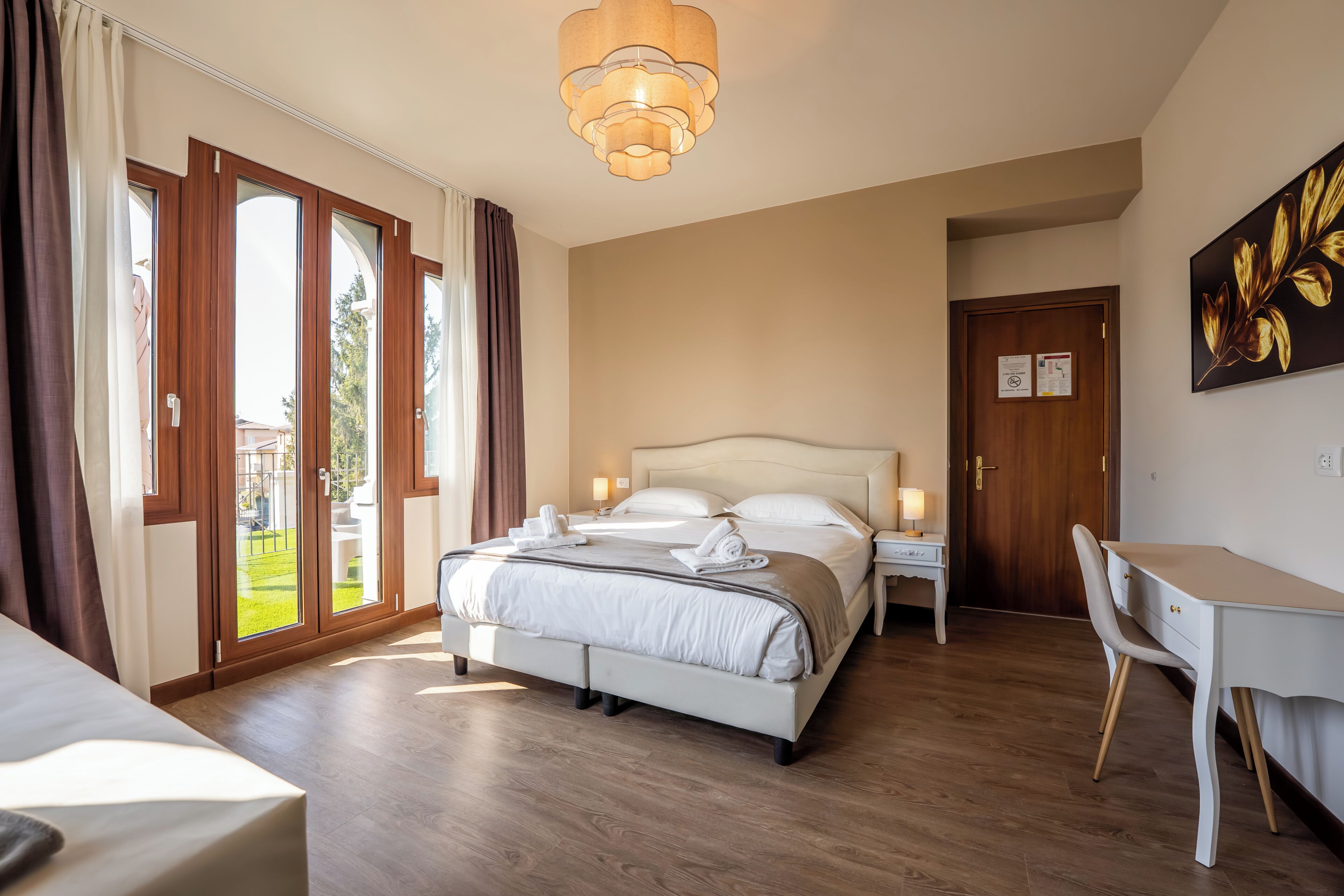 A hotel room with a bed, a desk, a chair, a chandelier, and a door.