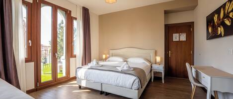 A hotel room with a bed, a desk, a chair, a chandelier, and a door.