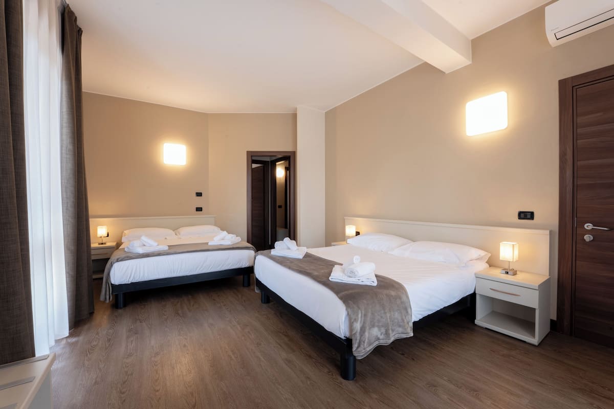 Quarto de hotel com duas camas, mesas de cabeceira com abajures, uma porta e um ar condicionado na parede.