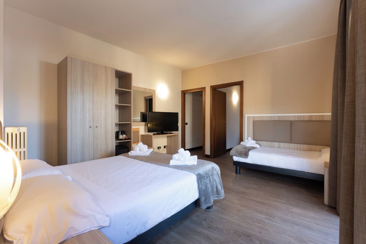 Quarto de hotel com duas camas, televisão, guarda-roupa e banheiro.