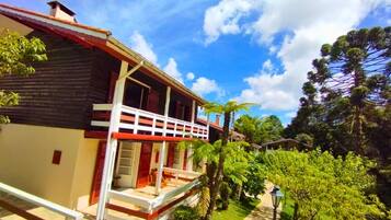 A two-story building with a balcony, surrounded by lush greenery and tall trees.