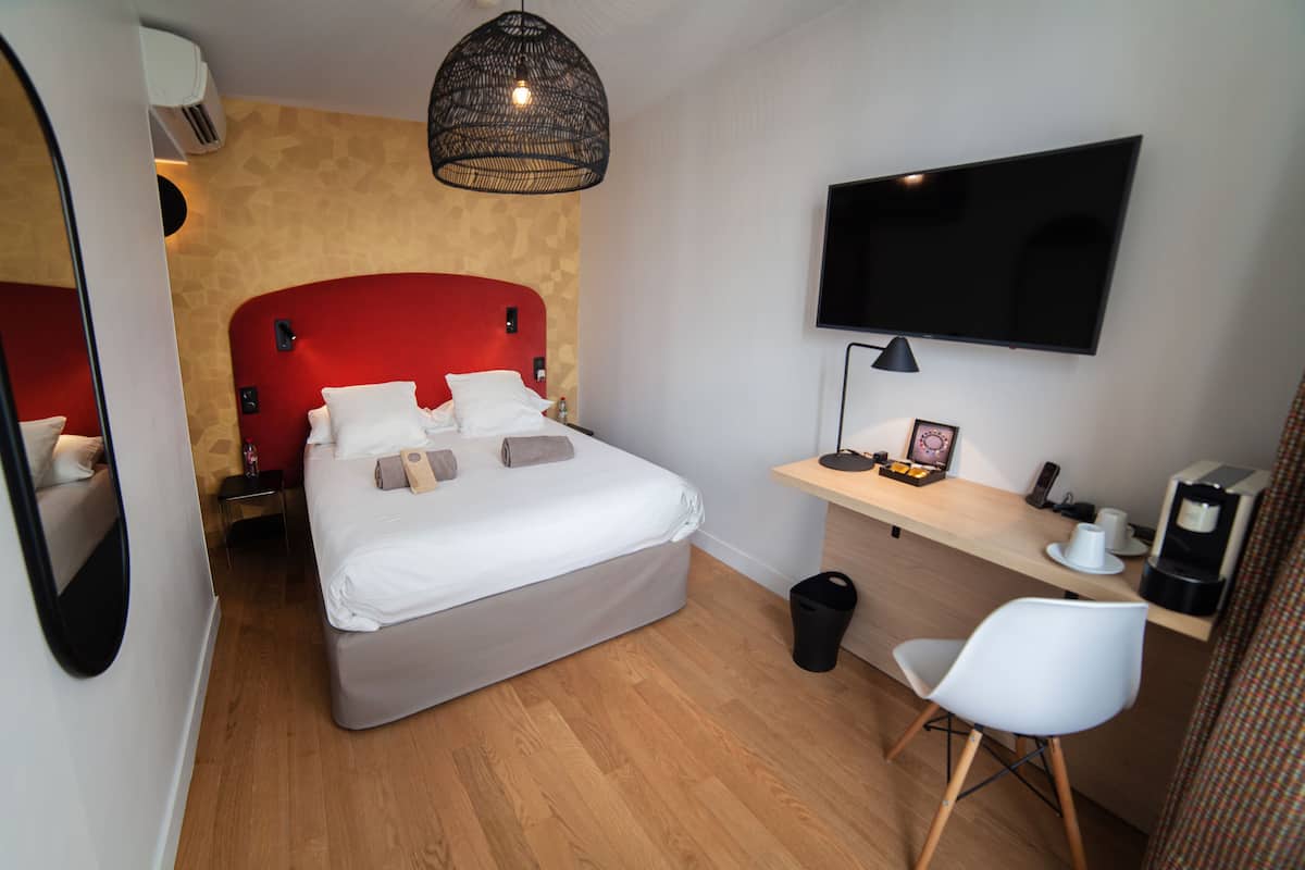A modern hotel room with a large bed, a desk with a computer, a TV, and a coffee machine.