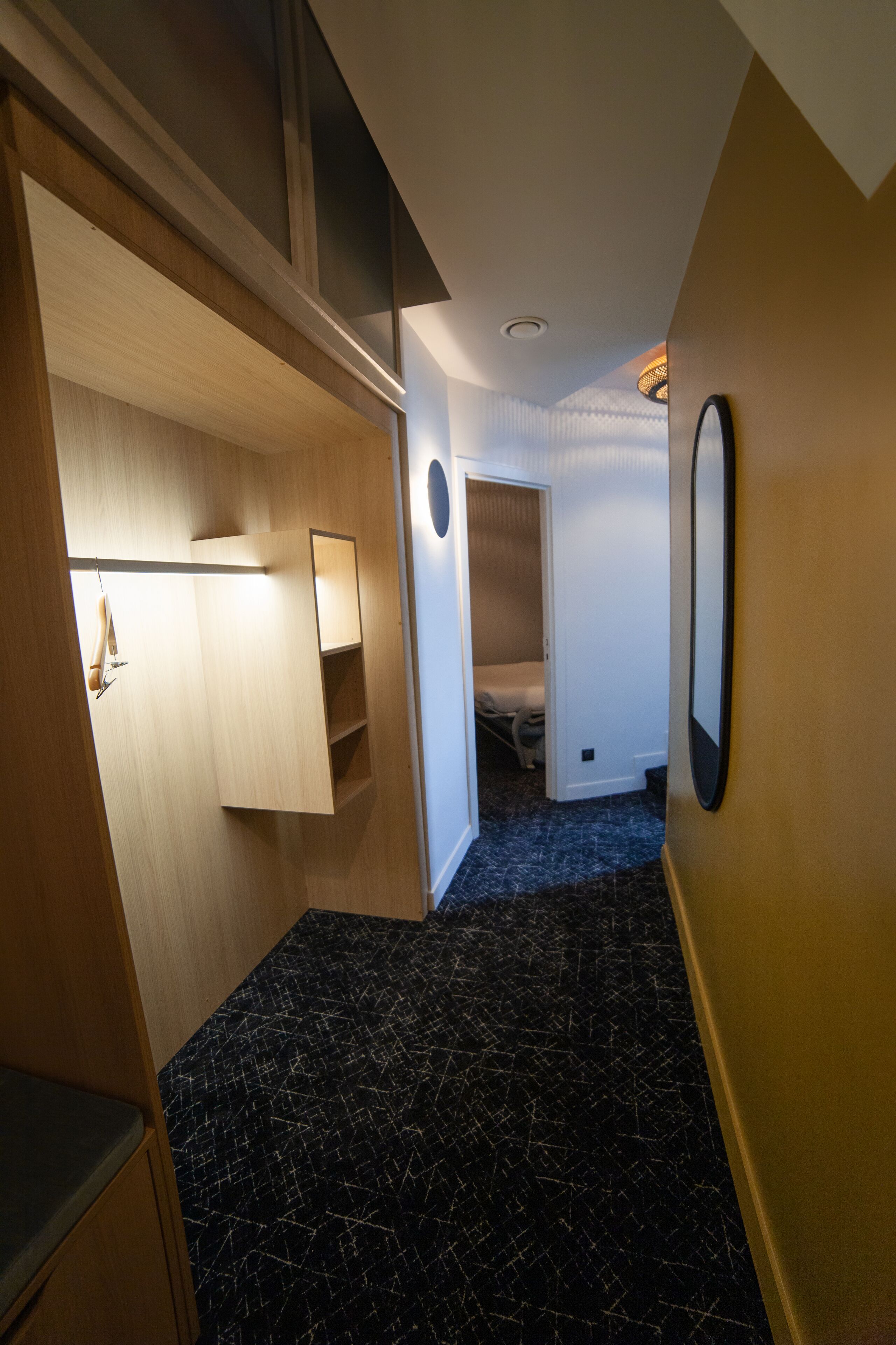 Un couloir avec une armoire en bois, un miroir et un lit dans la pièce adjacente.