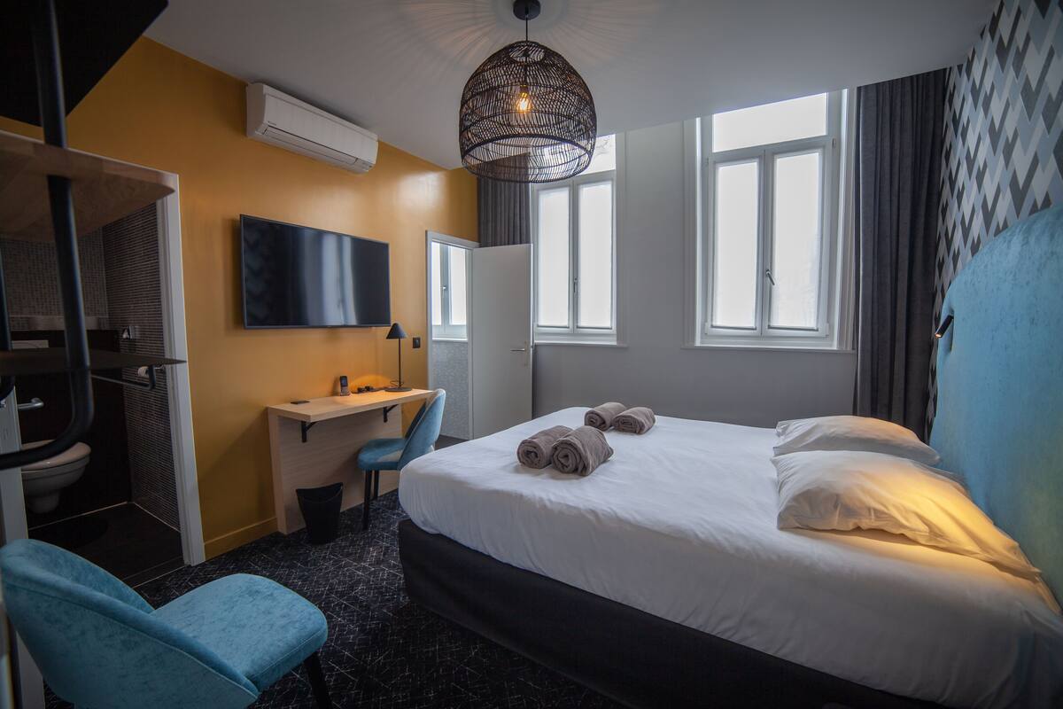 A hotel room with a bed, a desk, a chair, a TV, and a window.