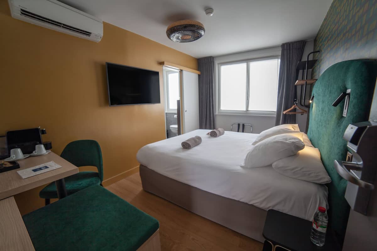 A hotel room with a bed, a desk, a chair, a TV, and a window.