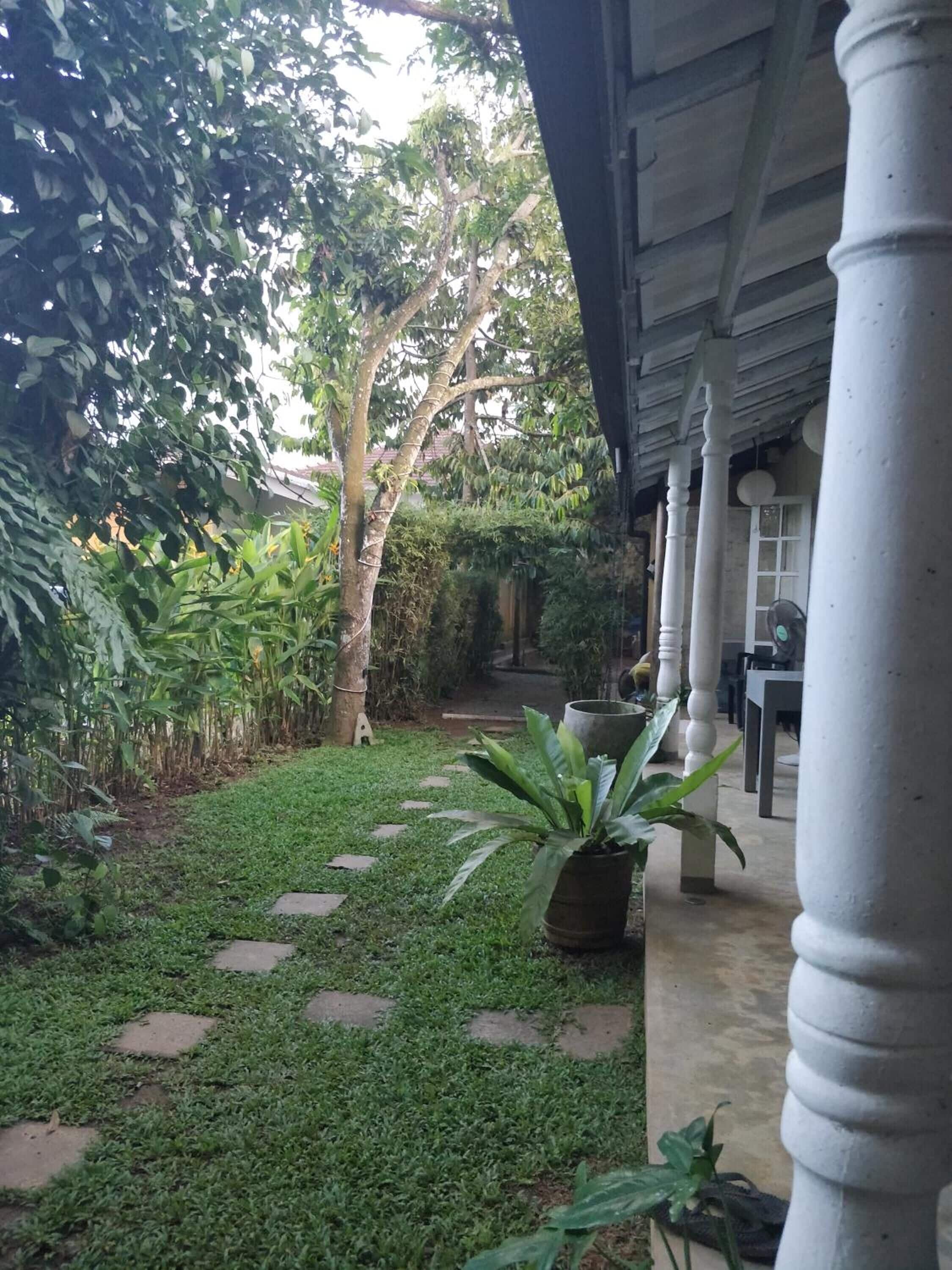 A covered outdoor area with a garden path, potted plants, and a building with columns.