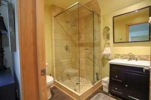 A bathroom with a glass-enclosed shower, a toilet, a sink with a mirror, and a dark-colored vanity.