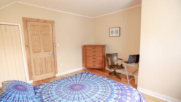 A bedroom with a bed, a wooden wardrobe, a desk with a chair, and a laptop.