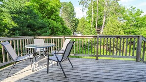 Une terrasse en bois avec une table ronde et deux chaises, entourée d’une balustrade en bois.