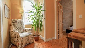 Une pièce chaleureuse avec un fauteuil à motifs floraux, une grande plante en pot et un plancher en bois.