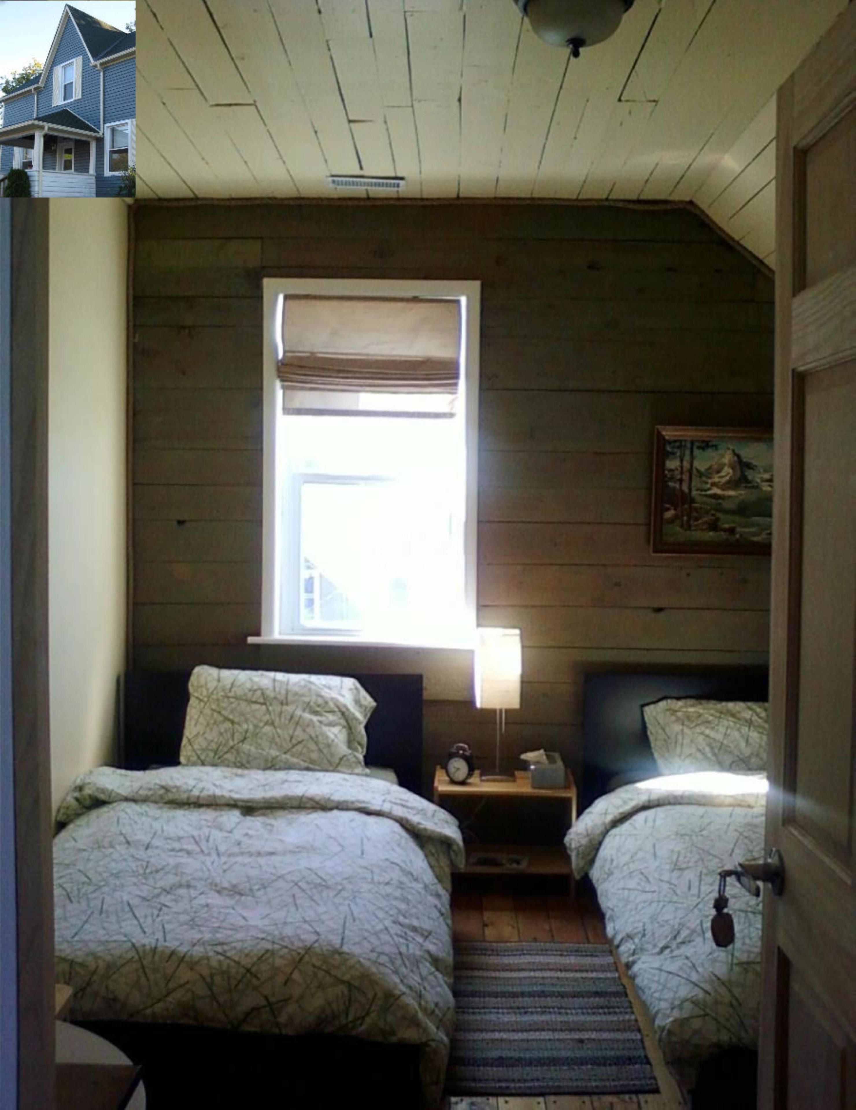 Une chambre avec deux lits, une fenêtre donnant sur un beau paysage, un tableau au mur et un plafond en bois.