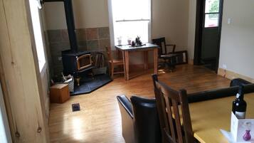 Una sala de estar acogedora con chimenea, piso de madera, una mesa de comedor y un sofá.