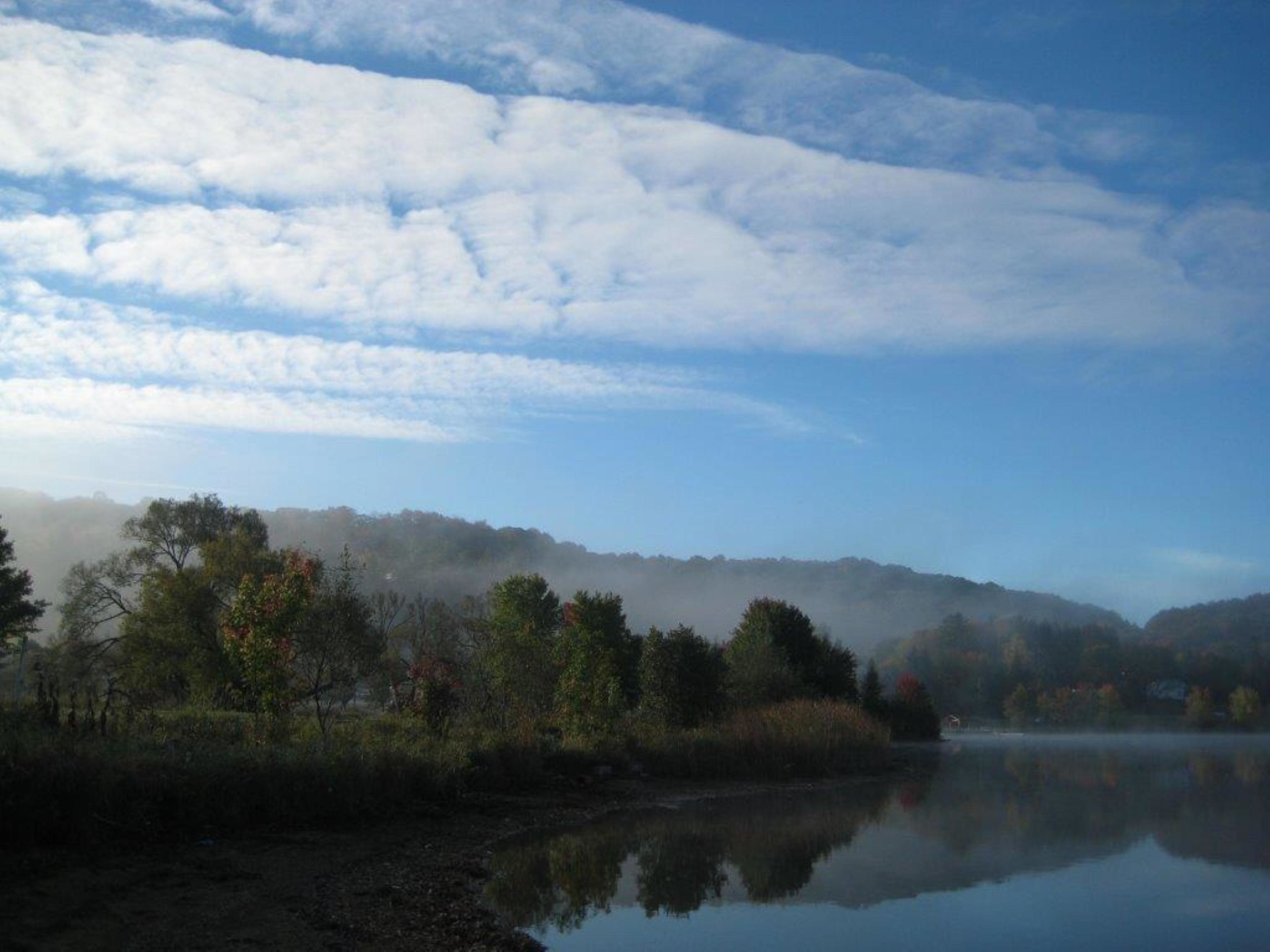 Un lago tranquilo con una colina boscosa y brumosa al fondo.