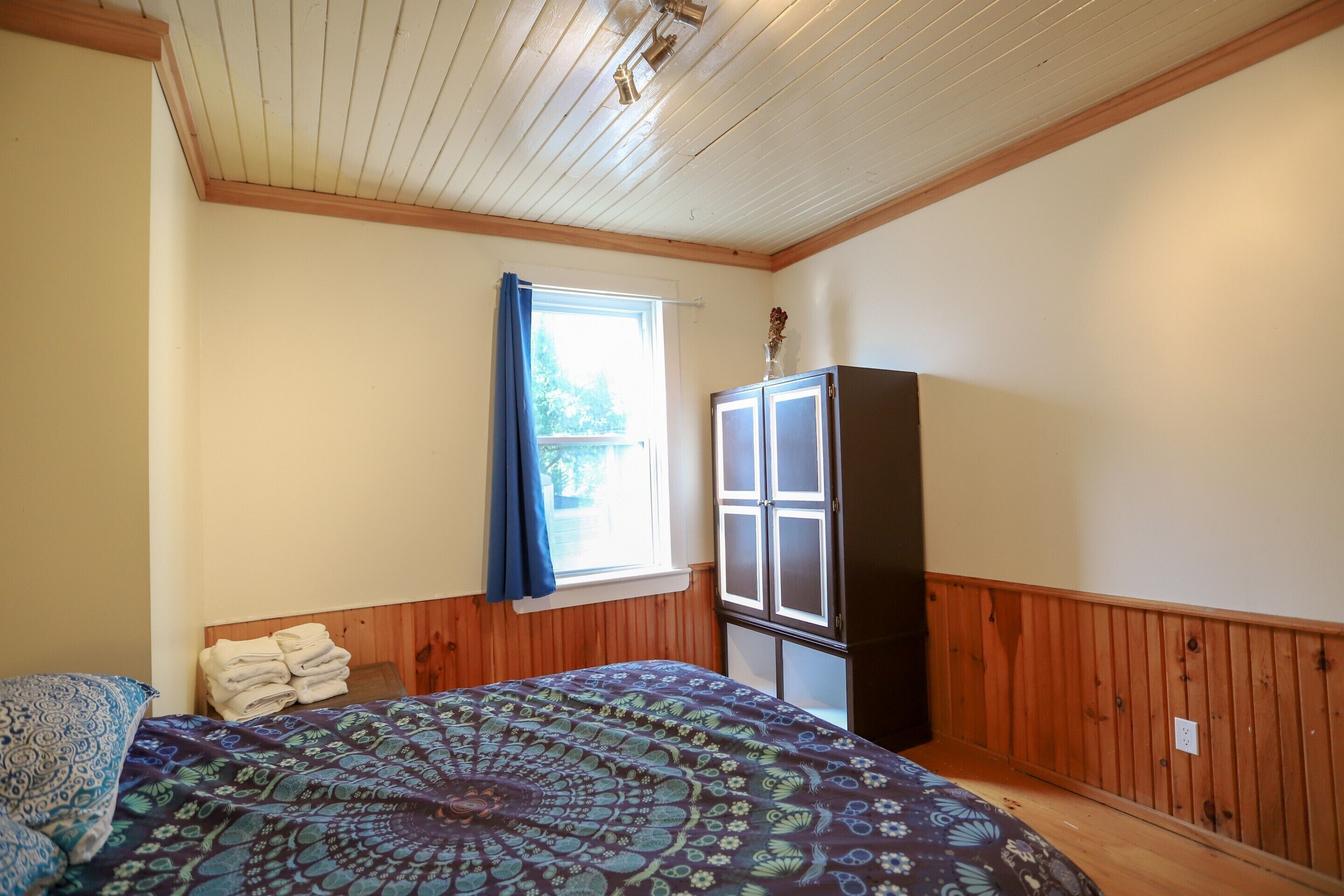 A bedroom with a bed, a window with curtains, a wardrobe, and a ceiling with wooden beams.