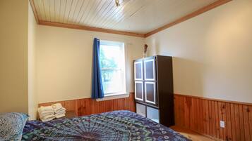 A bedroom with a bed, a window with curtains, a wardrobe, and a ceiling with wooden beams.