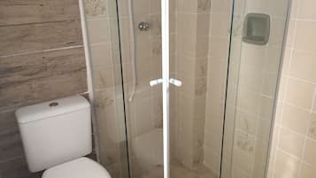 Une salle de bain comprenant des toilettes, une douche fermée par des parois en verre et des murs carrelés.