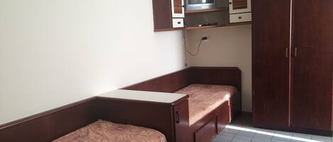 A small room with a bed, a wooden wardrobe, and a television on a shelf.