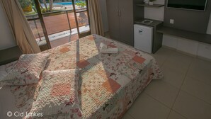 Une chambre avec un lit, un petit réfrigérateur, une télévision et une vue sur une piscine, visible par la fenêtre.