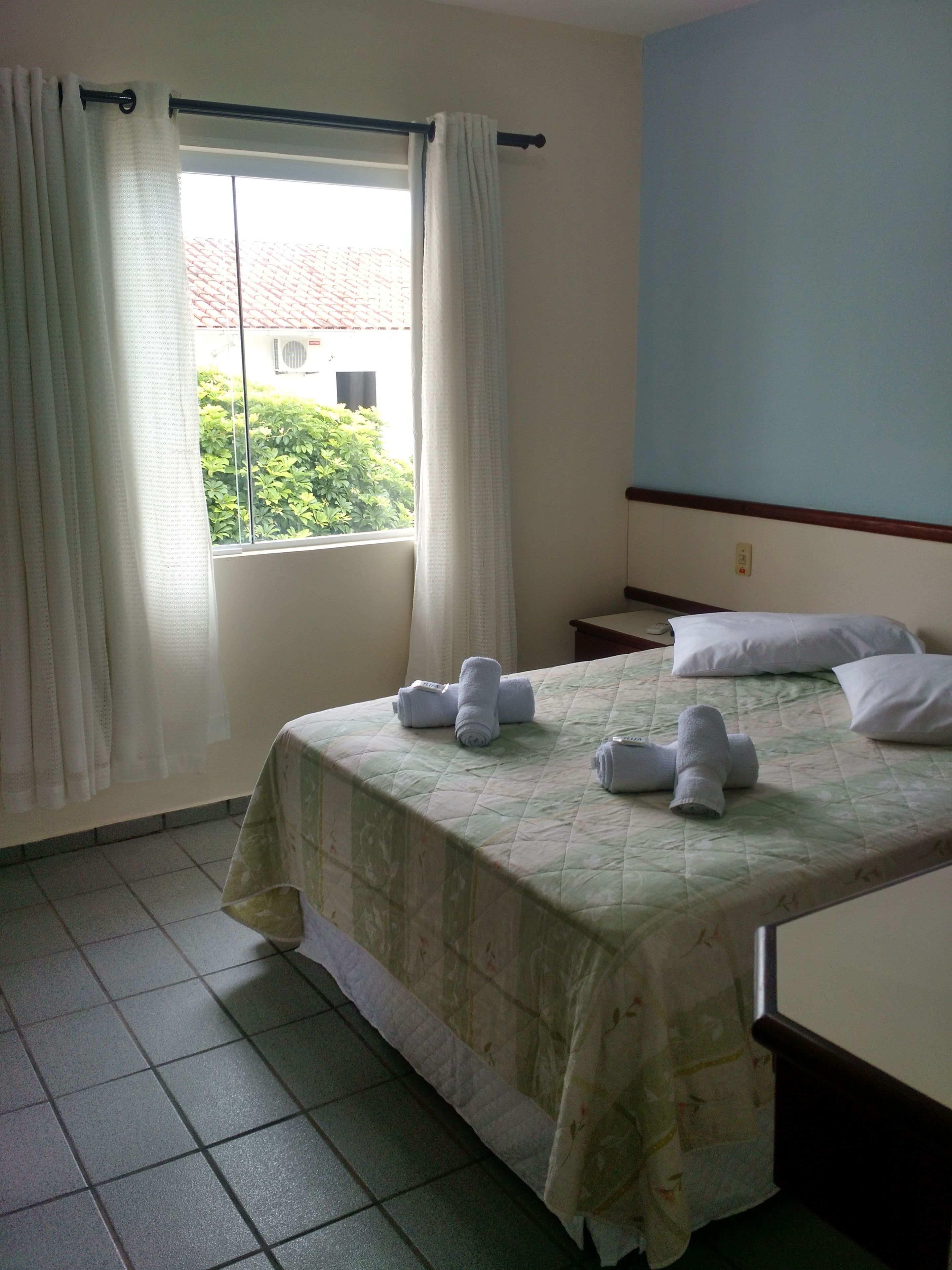 Une chambre d’hôtel avec un lit, une fenêtre avec des rideaux et une vue sur la verdure.