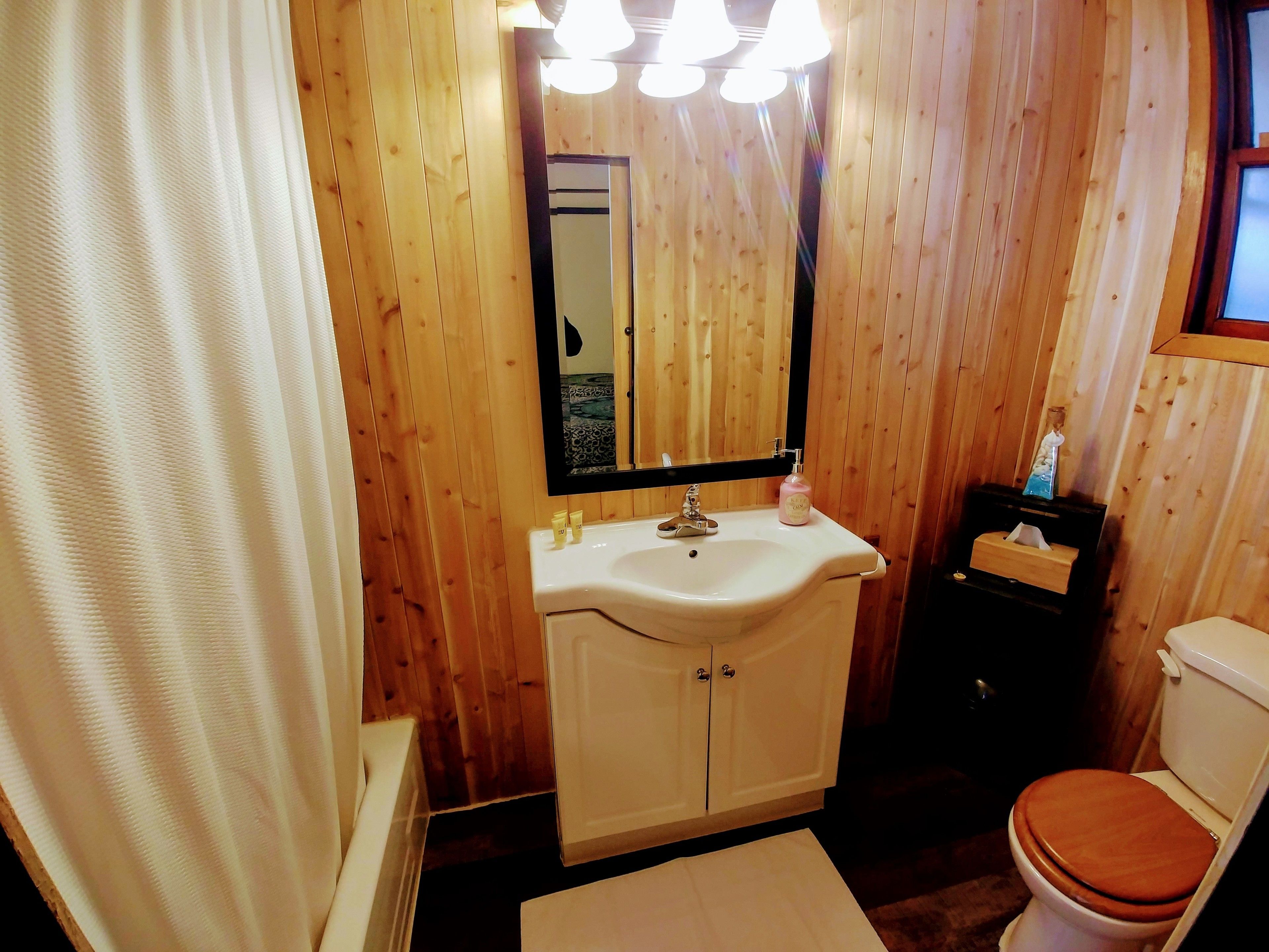 A wooden-paneled bathroom with a white sink, mirror, and wooden toilet.