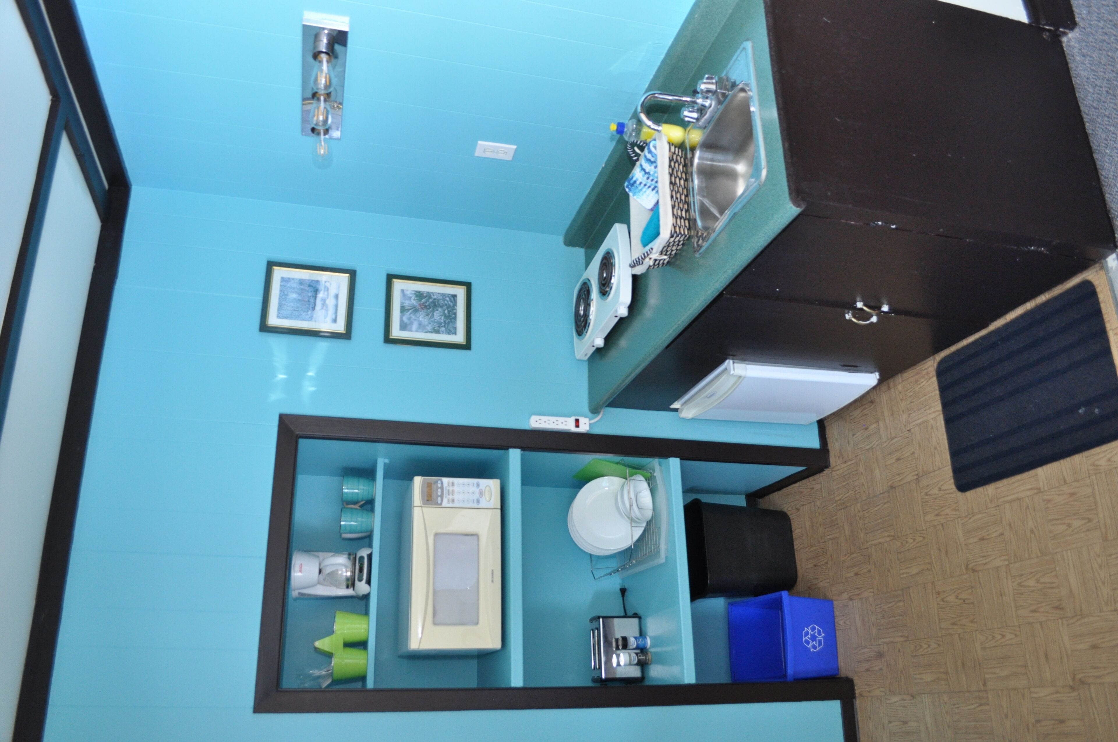 A kitchen with a microwave, toaster, and sink. There are framed pictures on the wall and a blue countertop.