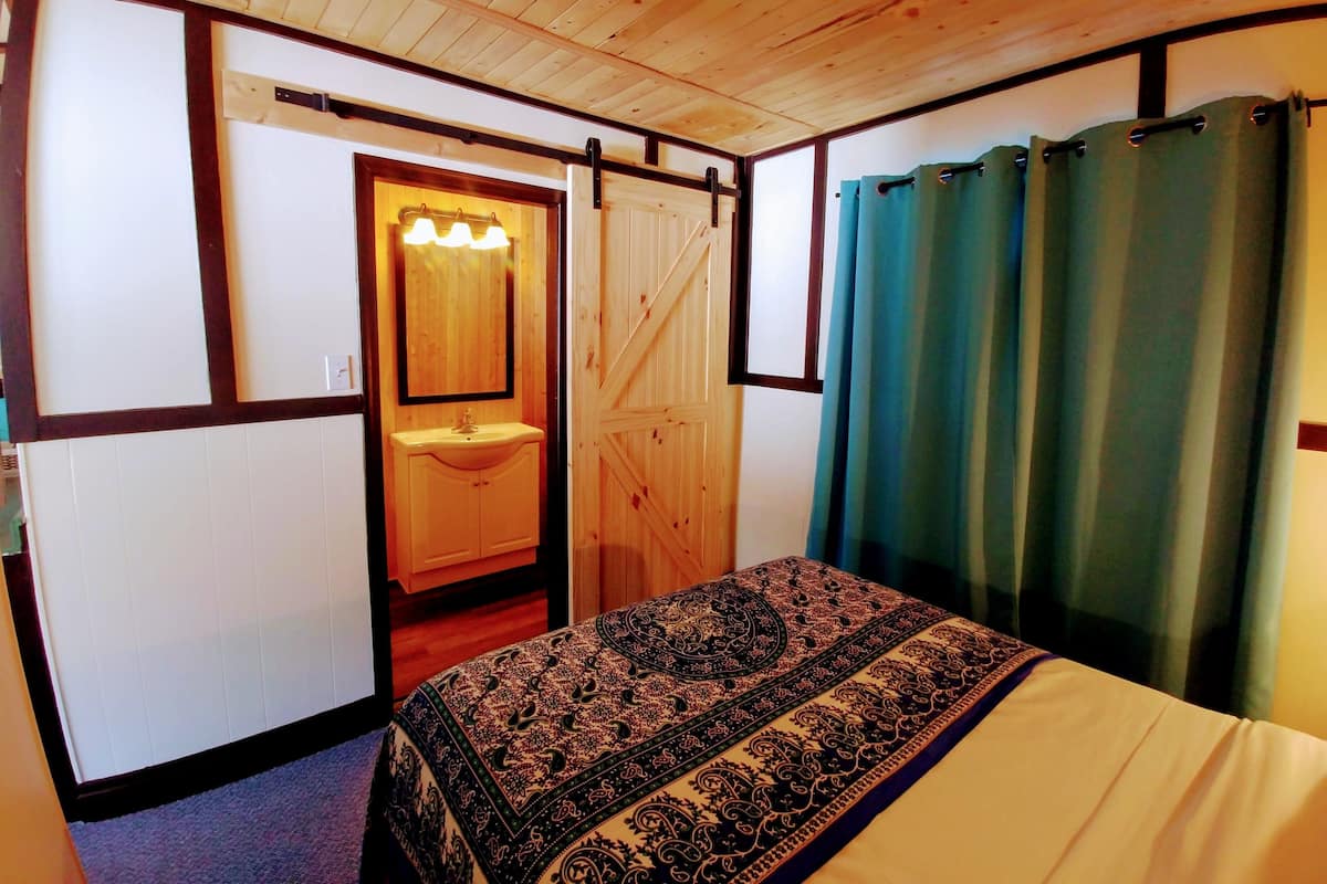 A room with a bed, a wooden door, a mirror, and a window with curtains.