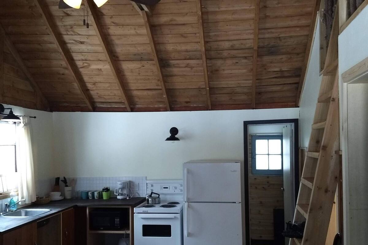 A kitchen with wooden beams, a ceiling fan, a refrigerator, an oven, and a microwave.