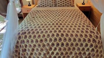 Una cama con una colcha estampada, un tapete rojo y beige, y un dosel sobre ella.