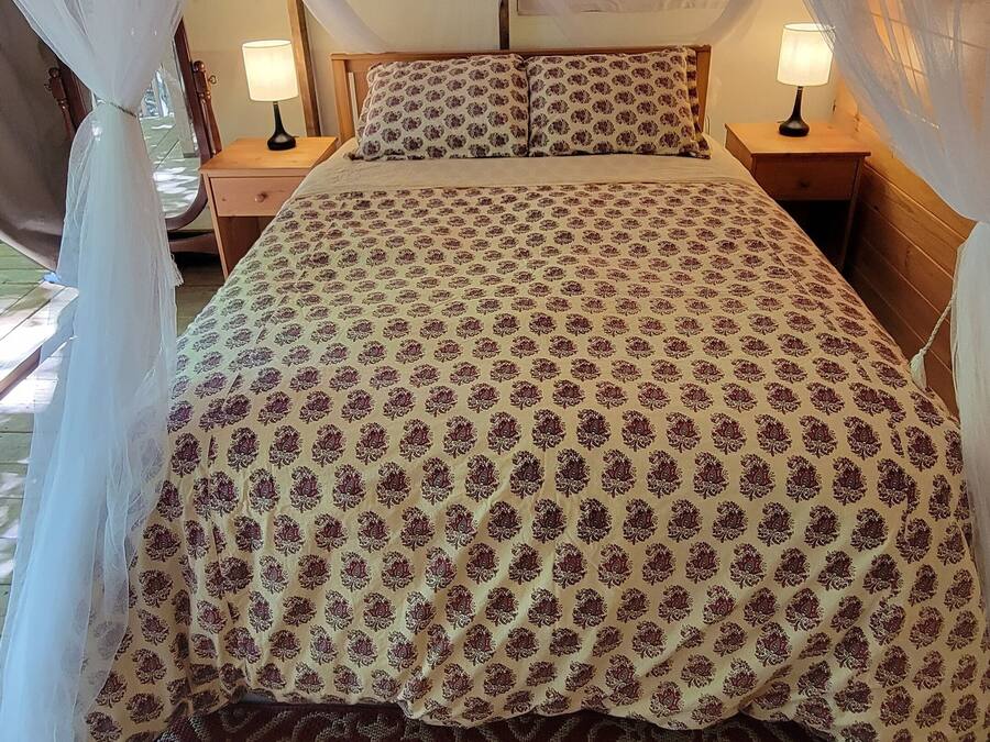 Una cama con una colcha estampada, un tapete rojo y beige, y un dosel sobre ella.