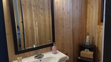 A bathroom with a wooden panel wall, a white sink with a mirror above it, and a wooden toilet.