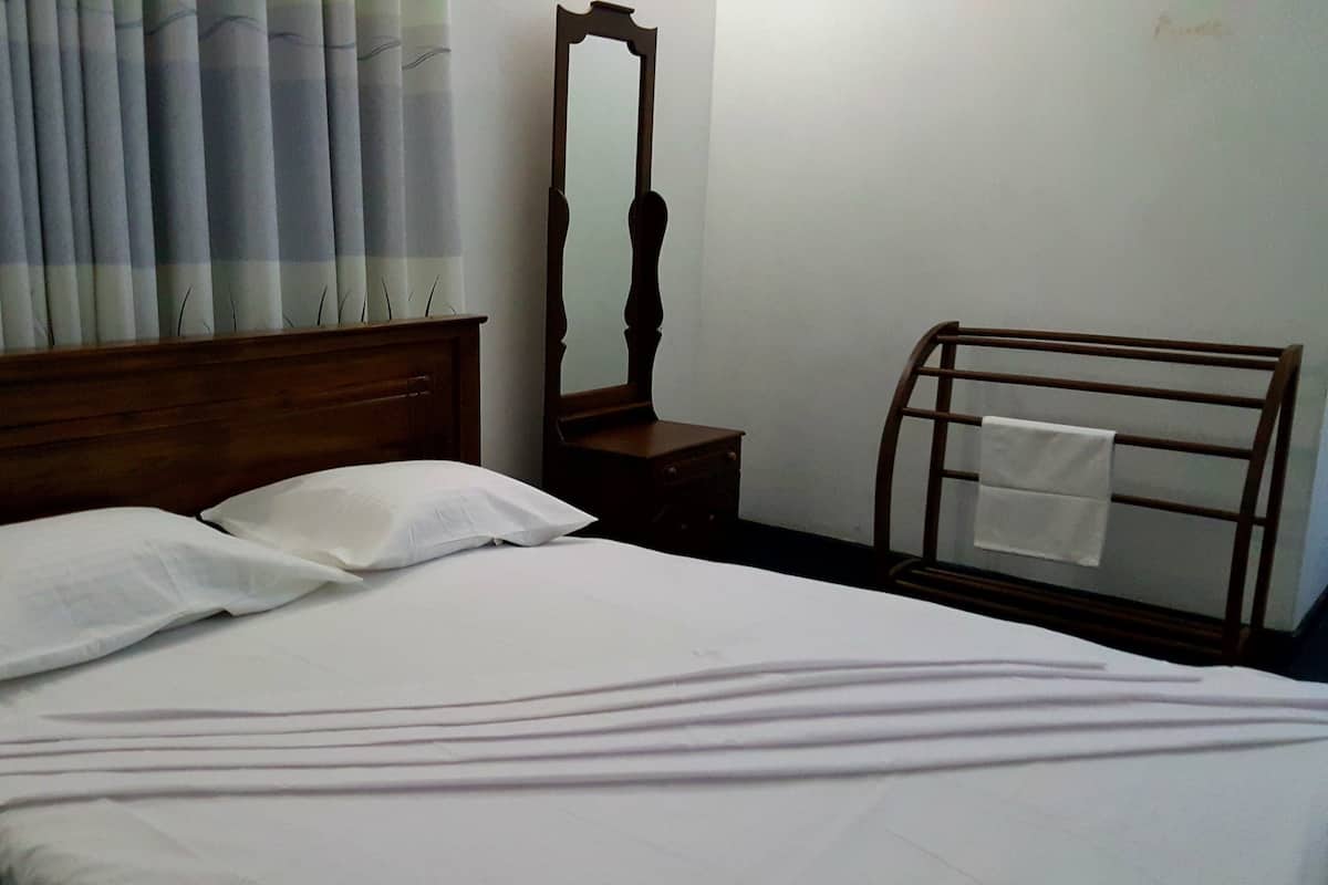 A neatly made bed with white linens and pillows, a wooden headboard, a wooden nightstand with a mirror, and a towel rack with a towel.