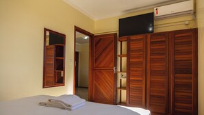 A hotel room with a bed, a wooden wardrobe, a mirror, and an air conditioning unit. - San Diego Apart Hotel (Florianopolis)