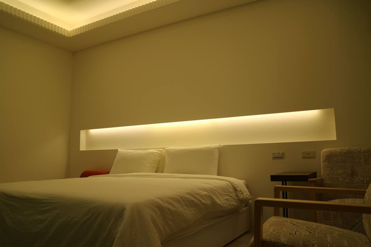 A hotel room with a bed, a nightstand, and a chair.