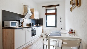 A modern kitchen with a dining area, wooden flooring, white cabinetry, and a hanging light fixture. - City Park Apartment 23 (Leipzig)