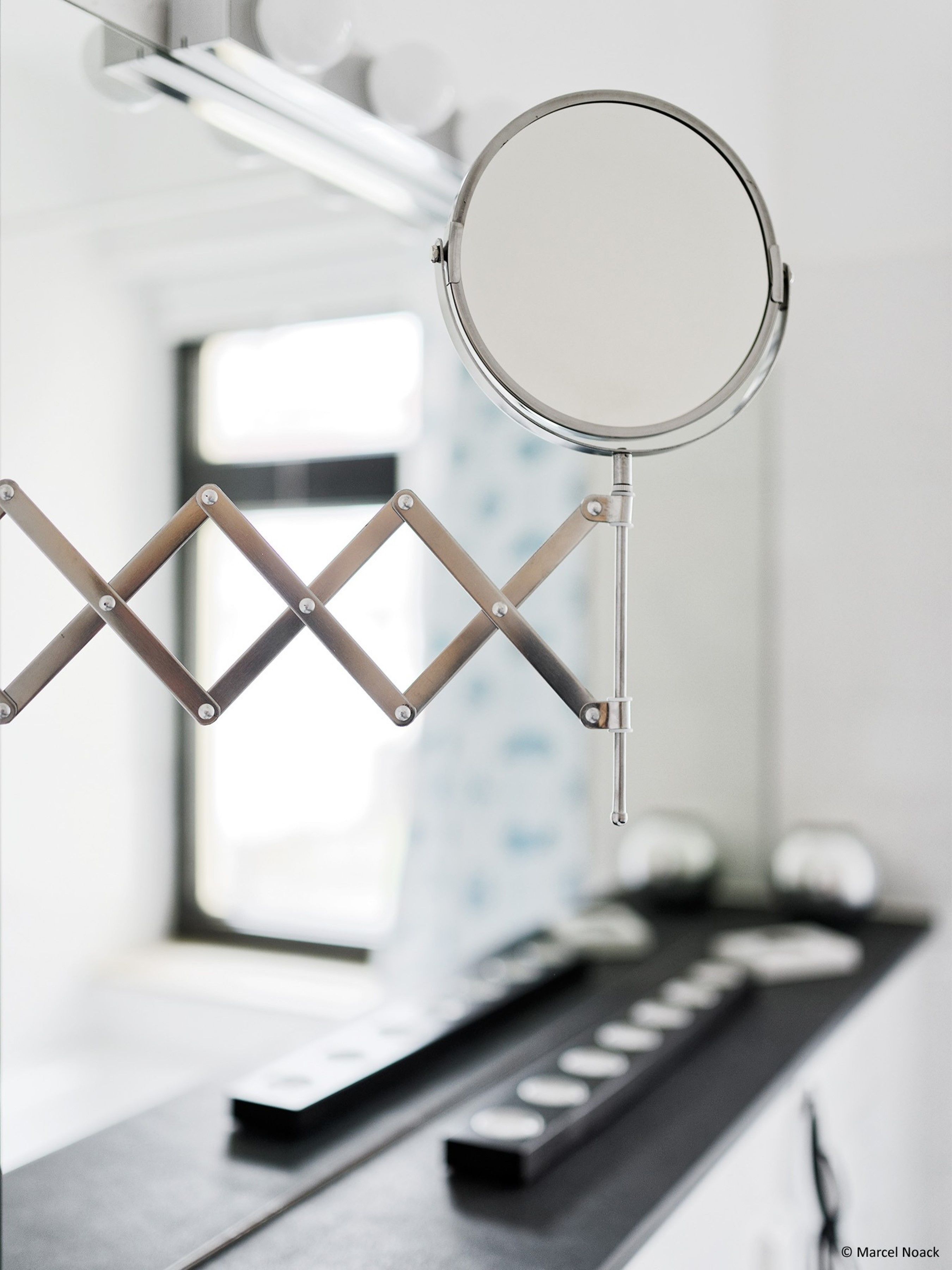 Un baño pequeño y moderno con un espejo sujeto a un soporte metálico.