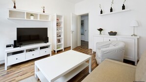 A modern living room with a flat-screen TV, white furniture, and a bookshelf. - City Park Apartment 23 (Leipzig)
