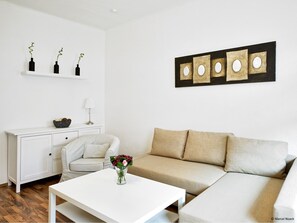 A modern living room with a sofa, a coffee table with a vase of flowers, a white cabinet, and a wall-mounted shelf with decorative bottles. - City Park Apartment 23 (Leipzig)