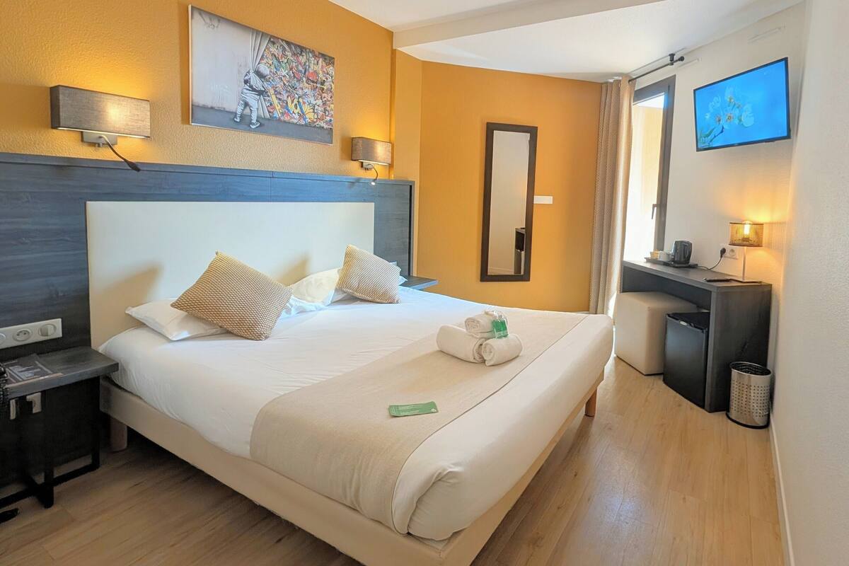 Una habitación de hotel con una cama grande, mesitas de noche, un escritorio, un espejo y un televisor.
