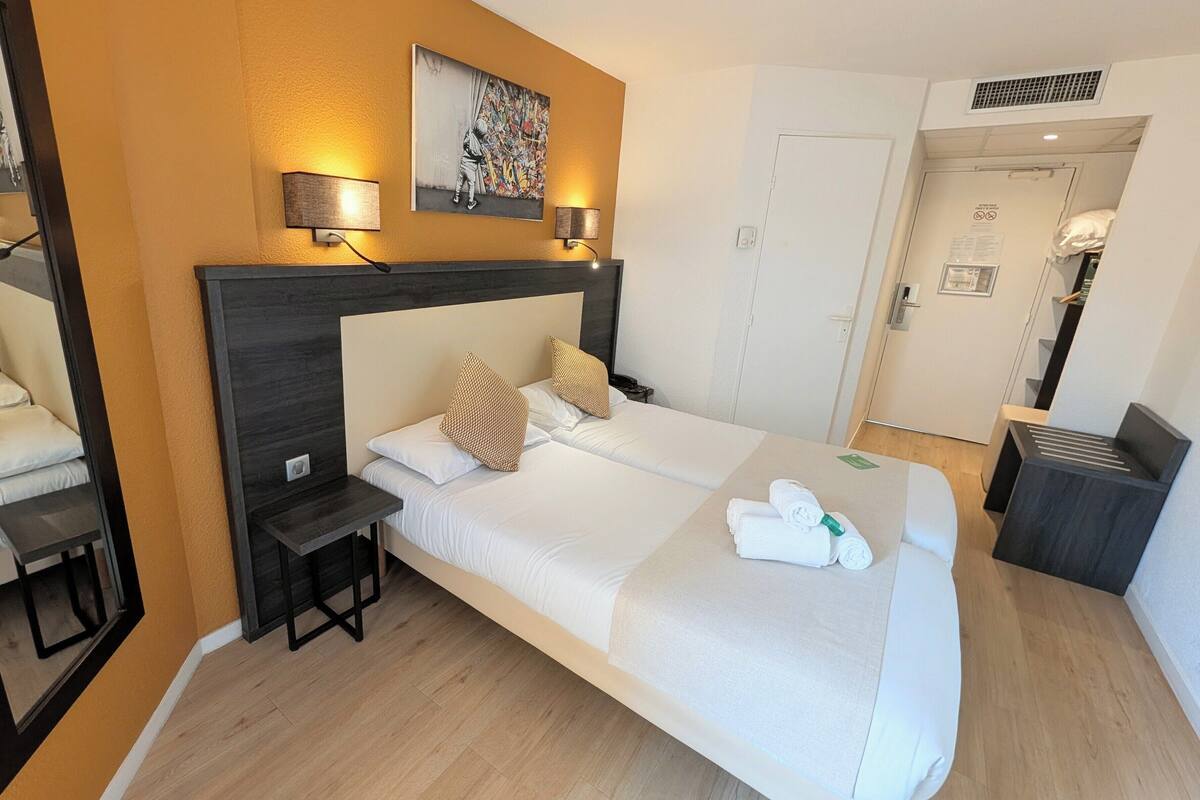 Una habitación de hotel con una cama grande, mesitas de noche, un escritorio y un cuadro en la pared.