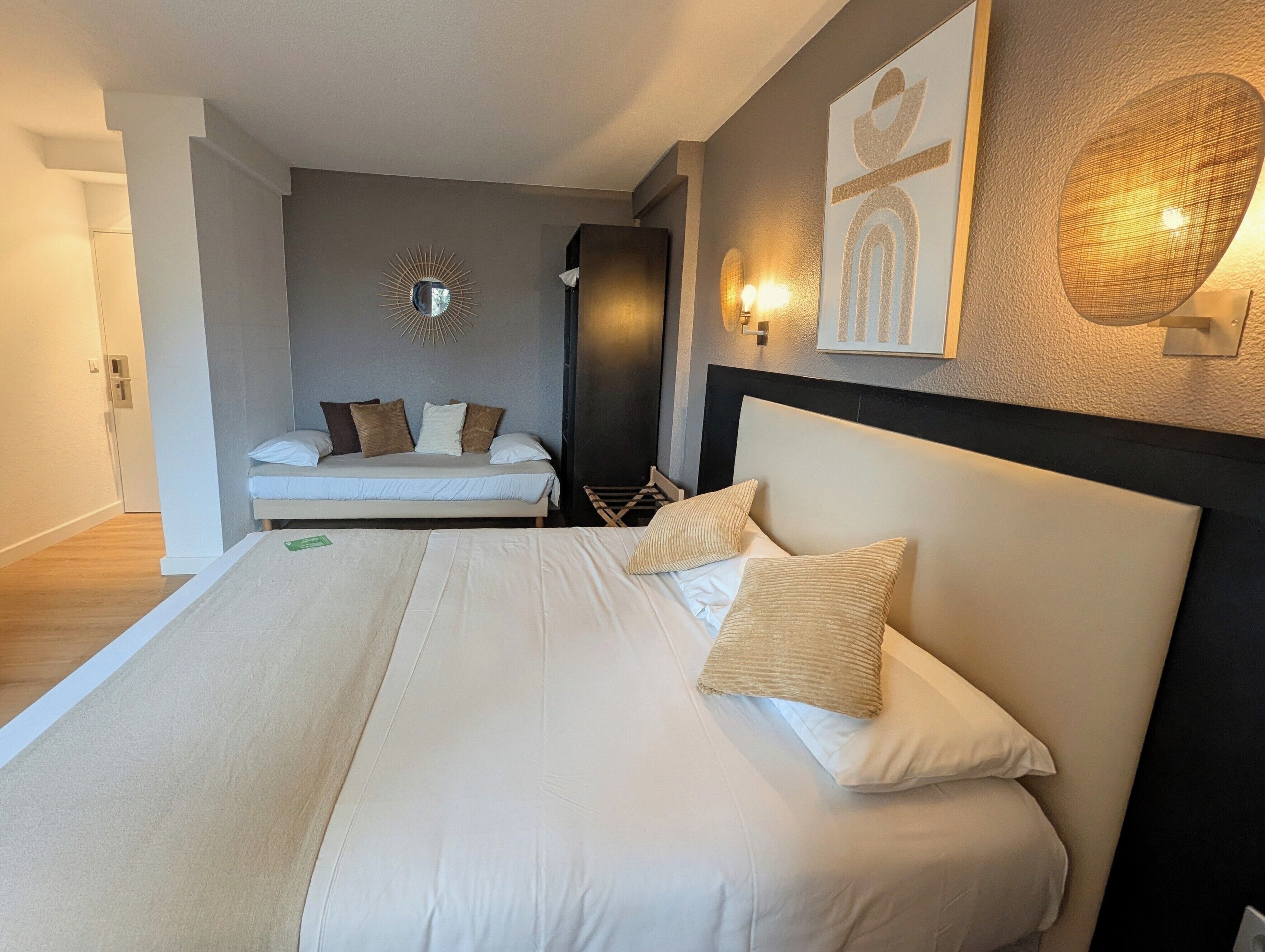 A hotel room with a large bed, a wall-mounted mirror, and a wall-mounted light fixture.