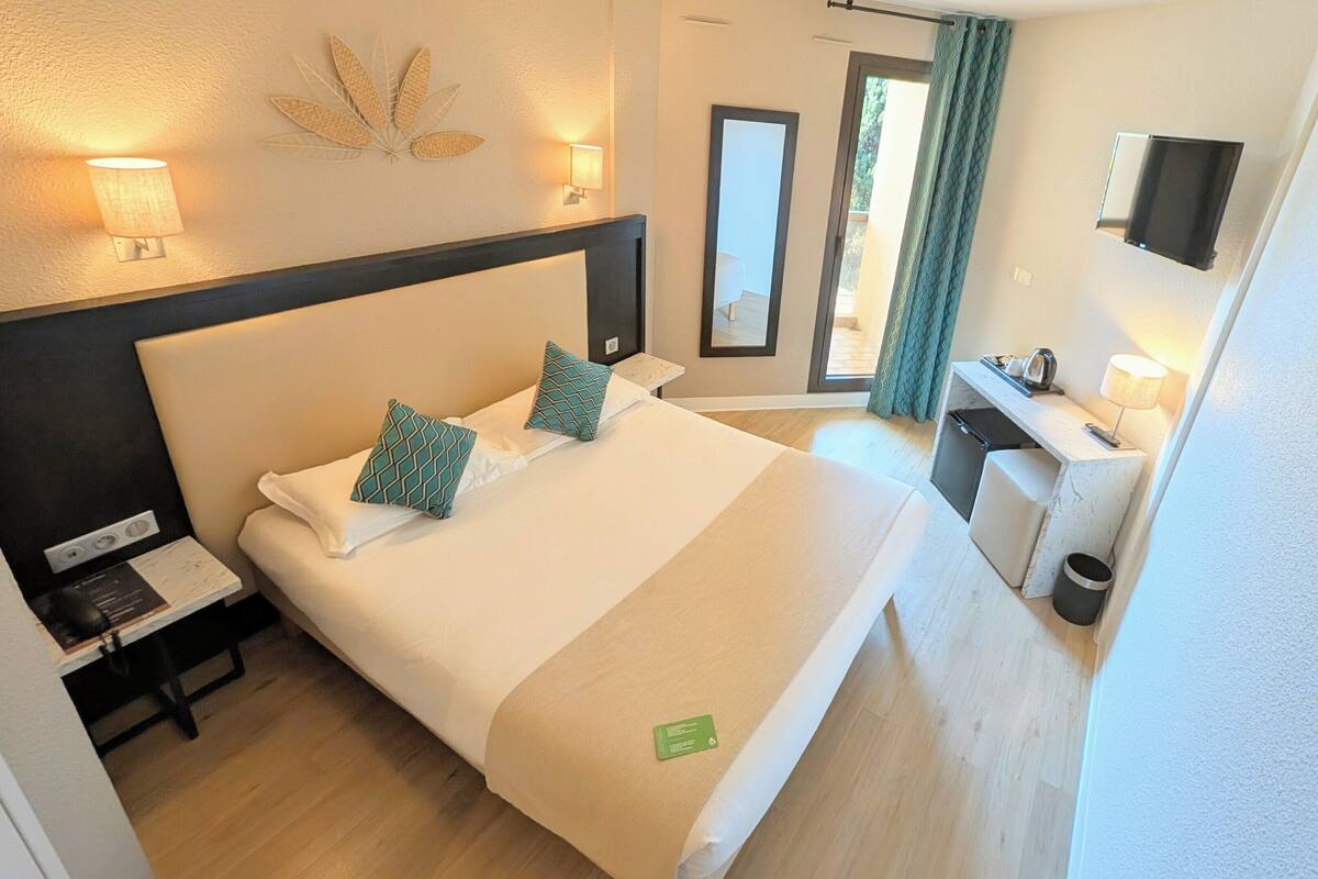 Habitación de hotel con cama, mesitas de noche, escritorio, espejo y televisión montada en la pared.